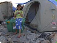 Ein Mädchen steht vor einer ShelterBox und einem Zelt daraus.