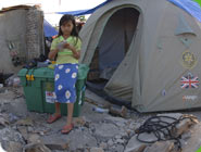 Ein M&auml;dchen steht vor einer ShelterBox und einem Zelt daraus.